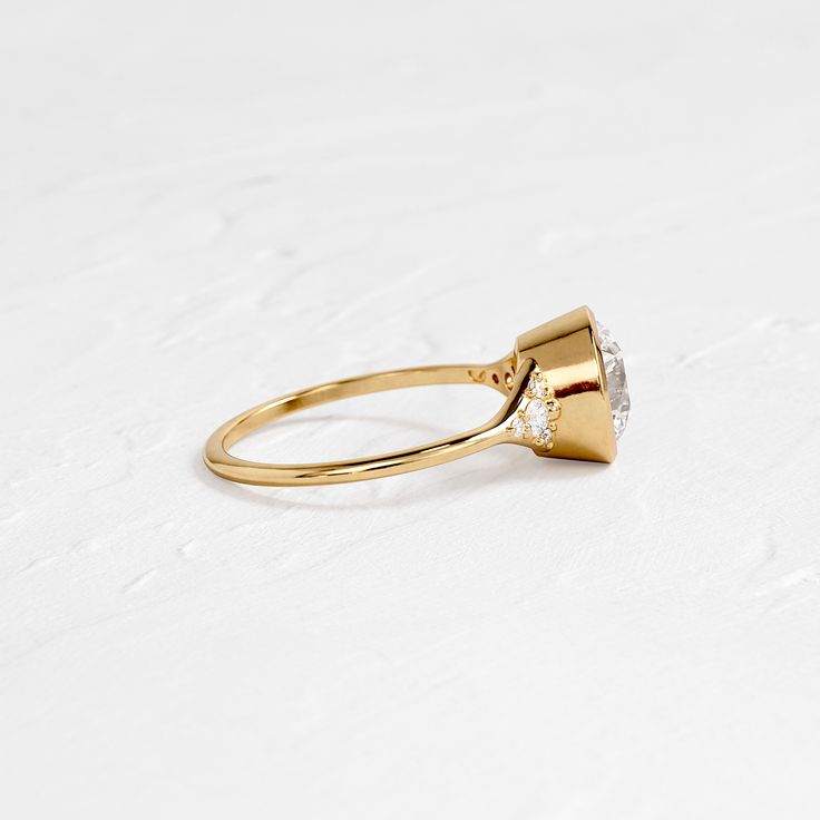 a yellow gold ring with a single diamond on the top, sitting on a white surface