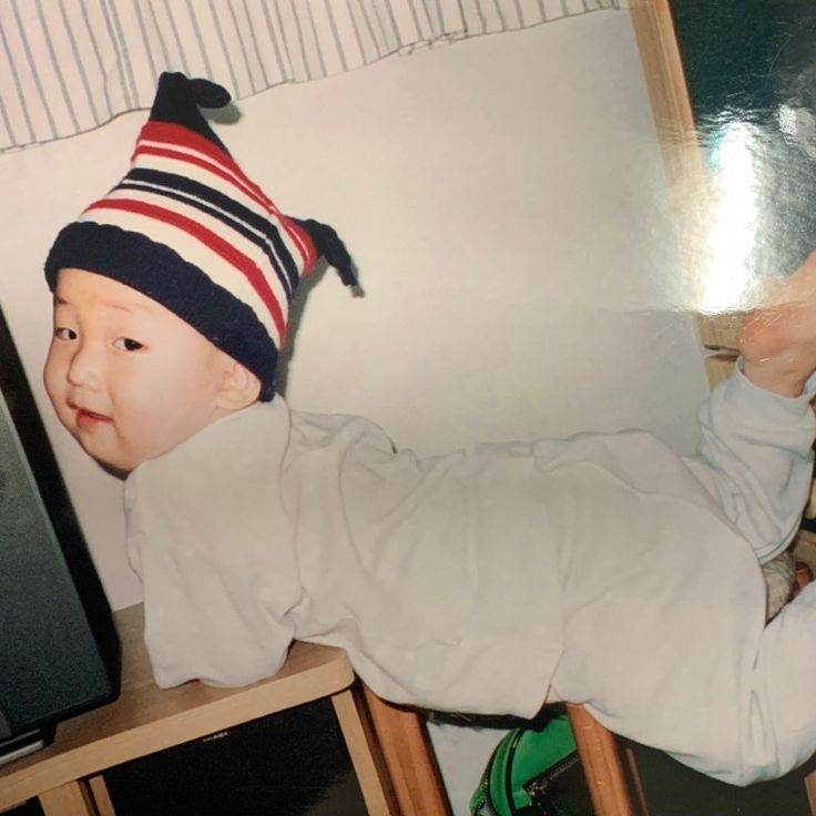 a baby wearing a hat laying on top of a wooden shelf next to a tv