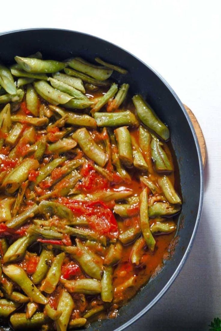 a pan filled with green beans and sauce on top of a white tablecloth next to a wooden spoon