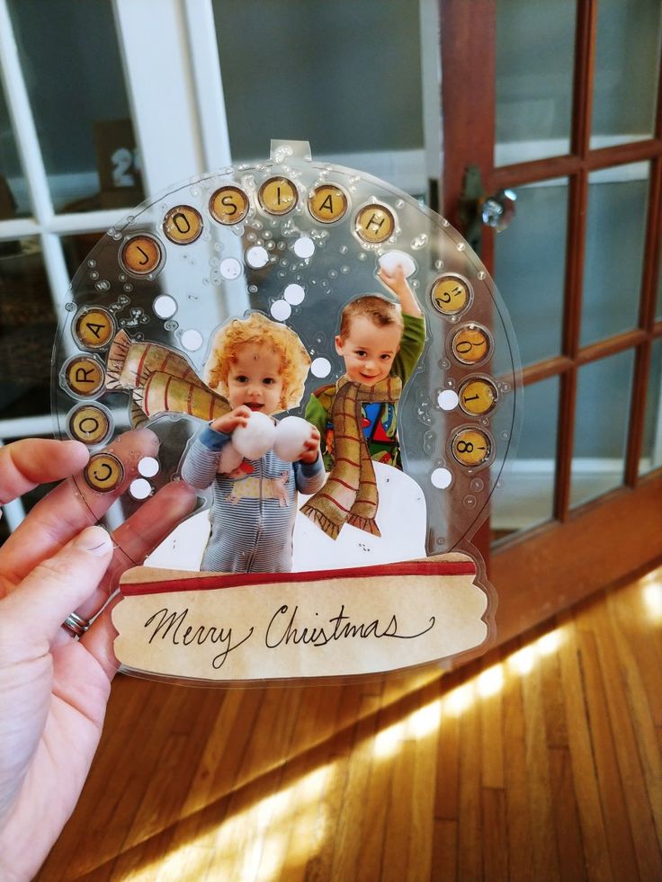 a hand holding a christmas ornament with two children