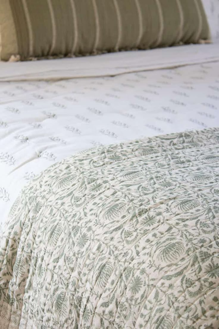 an unmade bed with green and white bedspread, pillows and throw pillow