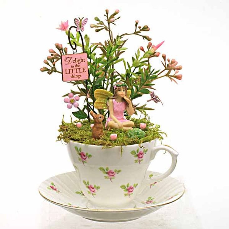 a teacup filled with flowers and a fairy figurine sitting on top of it