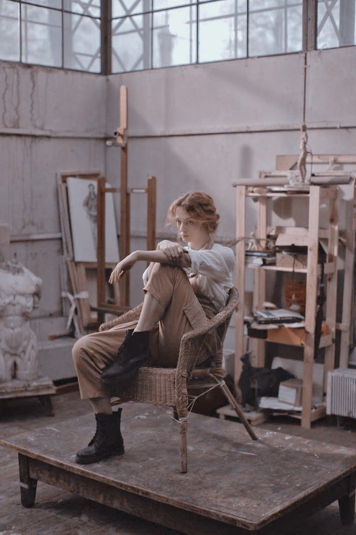 a woman sitting on top of a wooden chair in a room with lots of windows