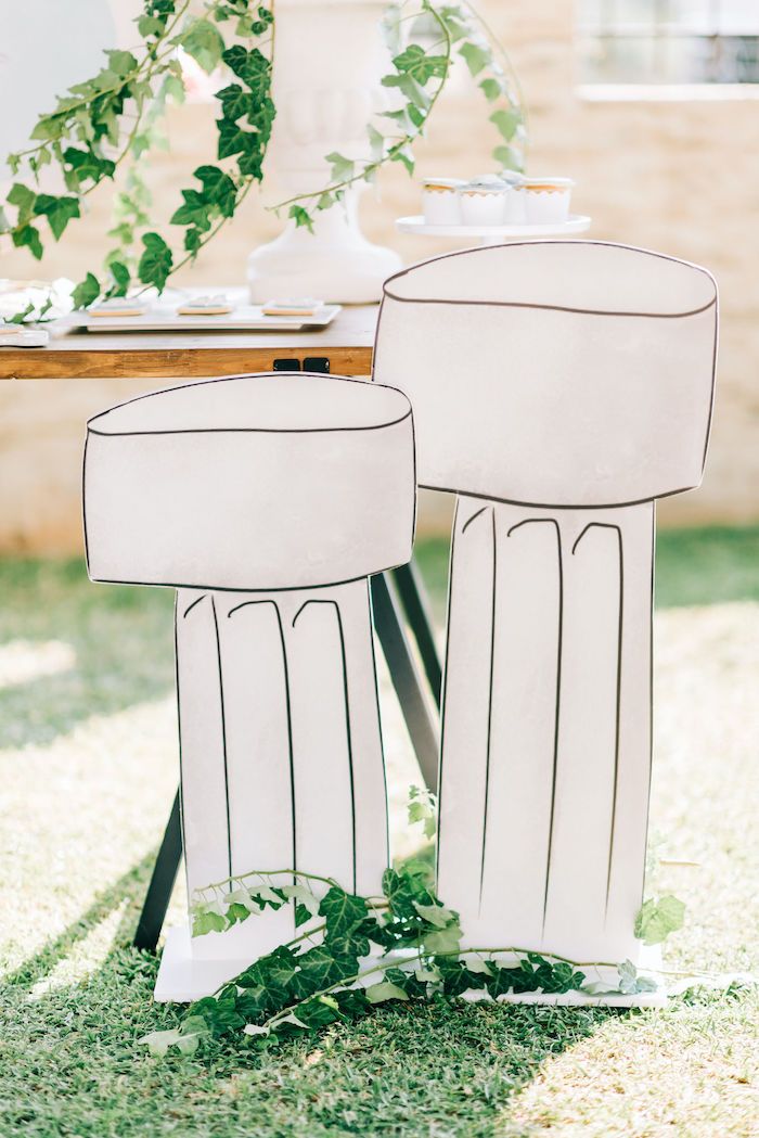 two white stools sitting on top of a grass covered field next to a table