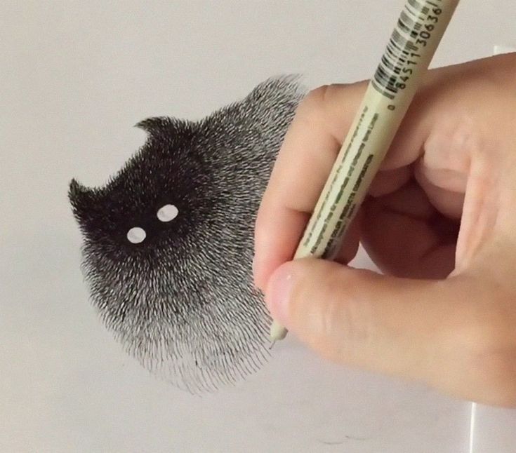 a hand holding a pencil and drawing a cat's face