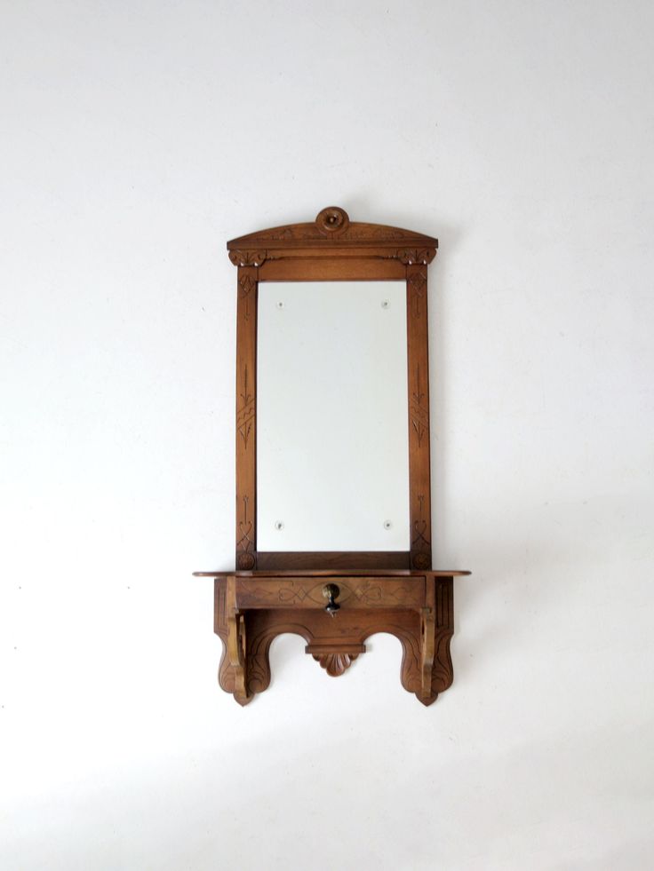 an old wooden mirror mounted to the side of a white wall next to a shelf