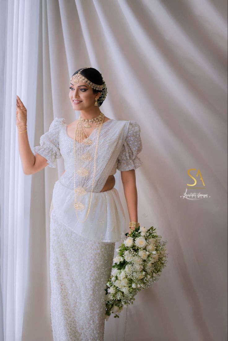 a woman wearing a white dress and holding a bouquet in her hand, standing next to a curtain