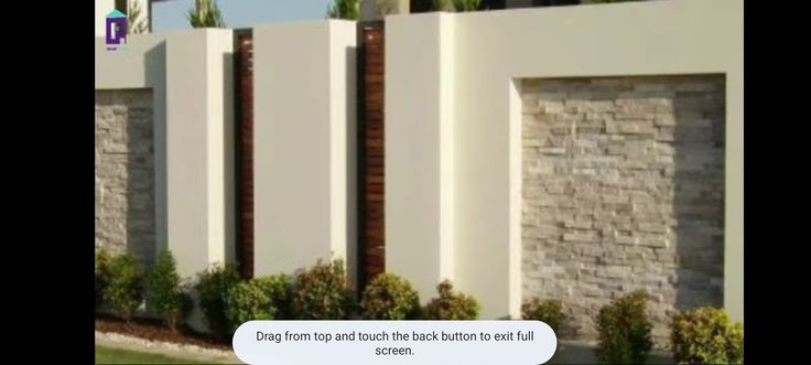 an image of a white fence with brick walls in the back ground and bushes on either side