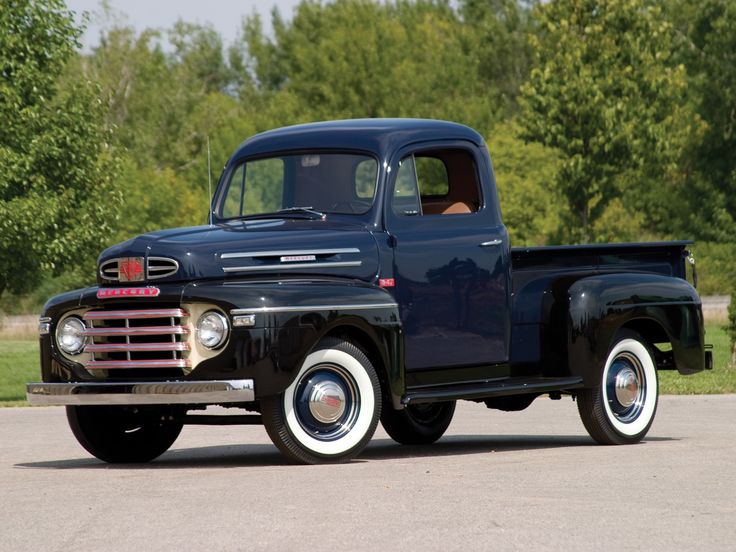 an old black pickup truck parked in a parking lot with trees in the back ground