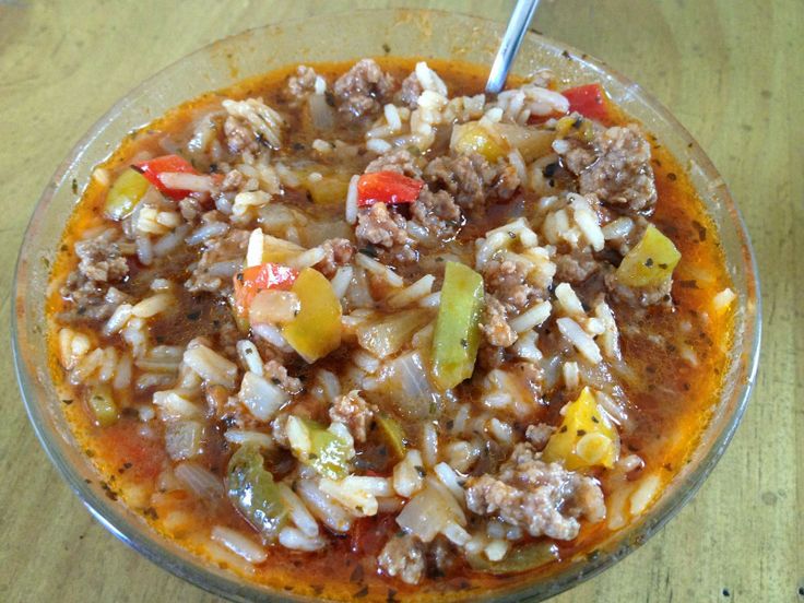 a bowl filled with rice and meat on top of a wooden table next to a fork