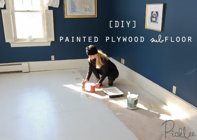 a woman is painting the floor in her living room with blue walls and white trim