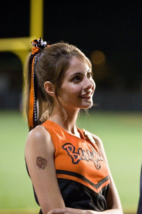 a woman in an orange and black cheerleader uniform standing on a baseball field at night