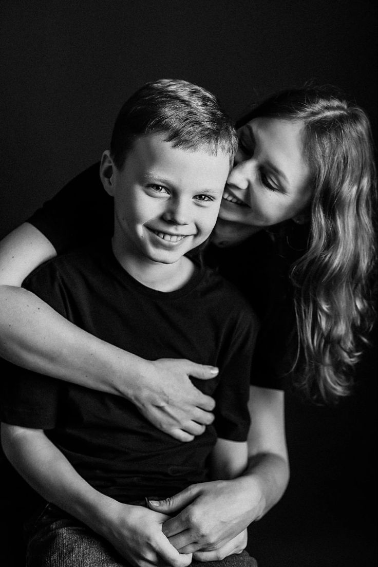 black and white photograph of a boy hugging his mother's shoulder in front of a dark background