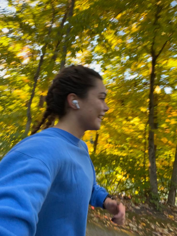 a man with ear buds on running in the park near some trees and leaves that are turning yellow