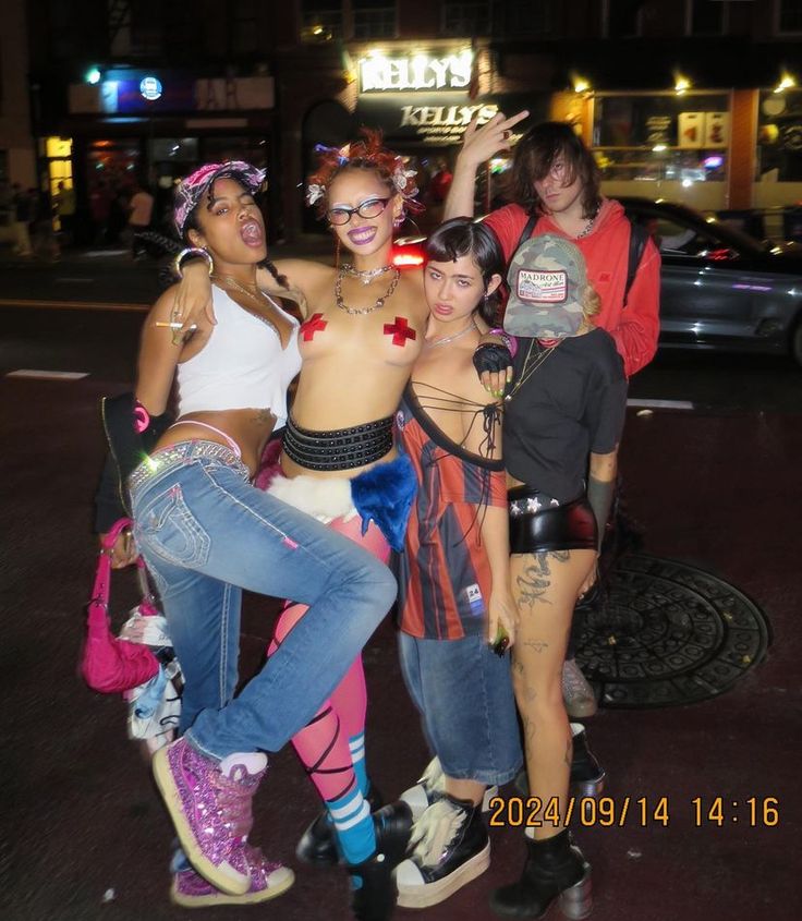 four women in costumes posing for the camera on a city street at night with their arms around each other