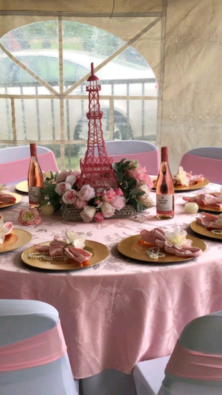 the table is set with pink and white plates, champagne bottles, and flowers in front of the eiffel tower