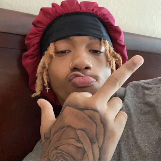 a young man with dreadlocks making the peace sign while wearing a bandana