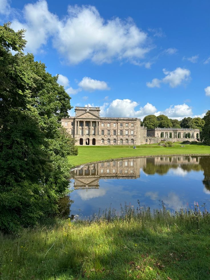 a large building sitting on the side of a lush green field next to a lake