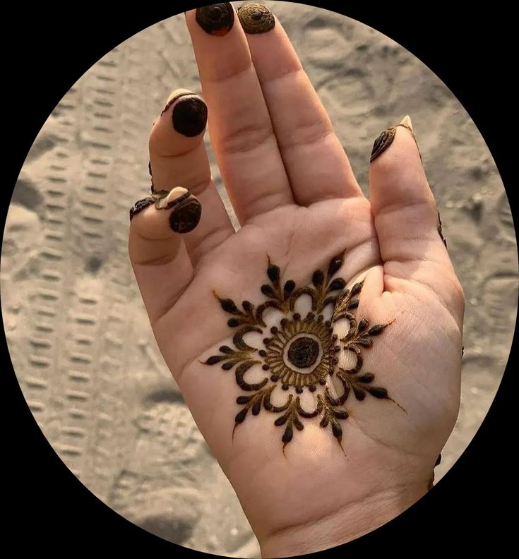 a woman's hand with a henna tattoo on it, in front of the sand