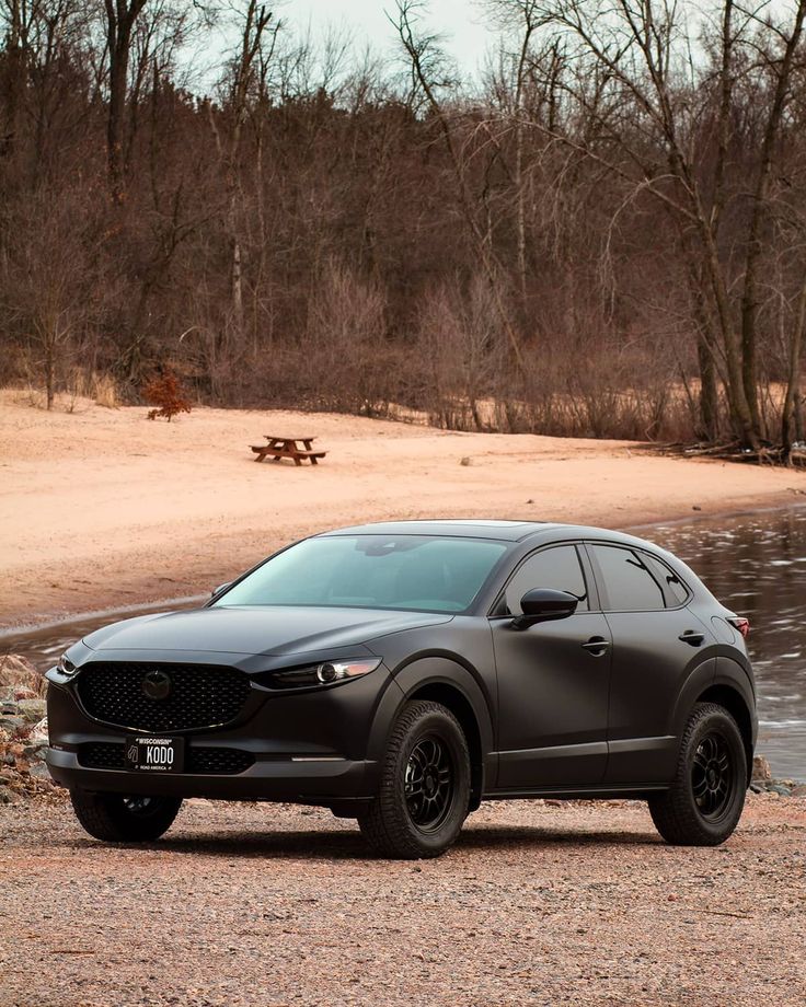 a black mazda cx - 30 parked in front of a lake and picnic table