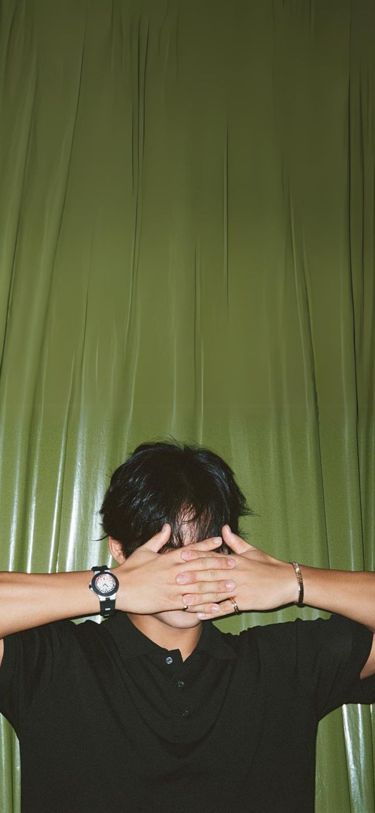 a man covering his face with his hands while standing in front of a green curtain