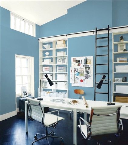 an office with dark green walls and white desks in the center is filled with bookshelves