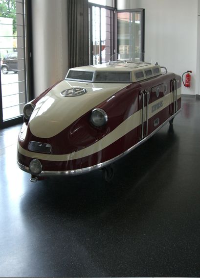 an old fashioned car is on display in a museum room with black floors and large windows