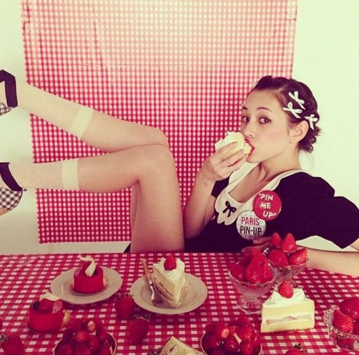 a woman sitting at a table eating cake and strawberries with her legs up on the table