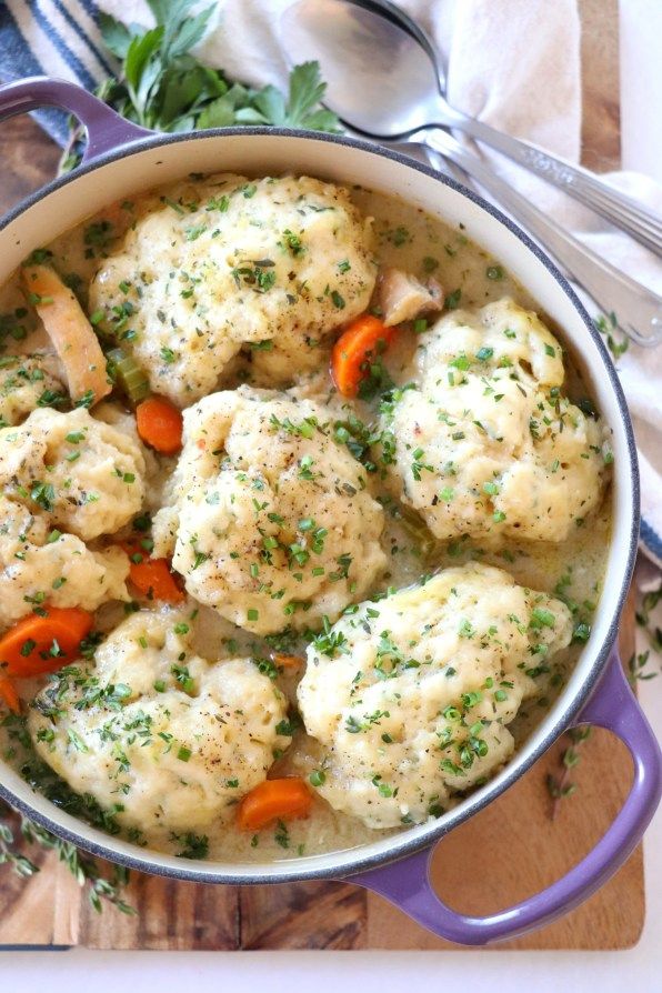 a pot filled with chicken and dumplings on top of a wooden cutting board