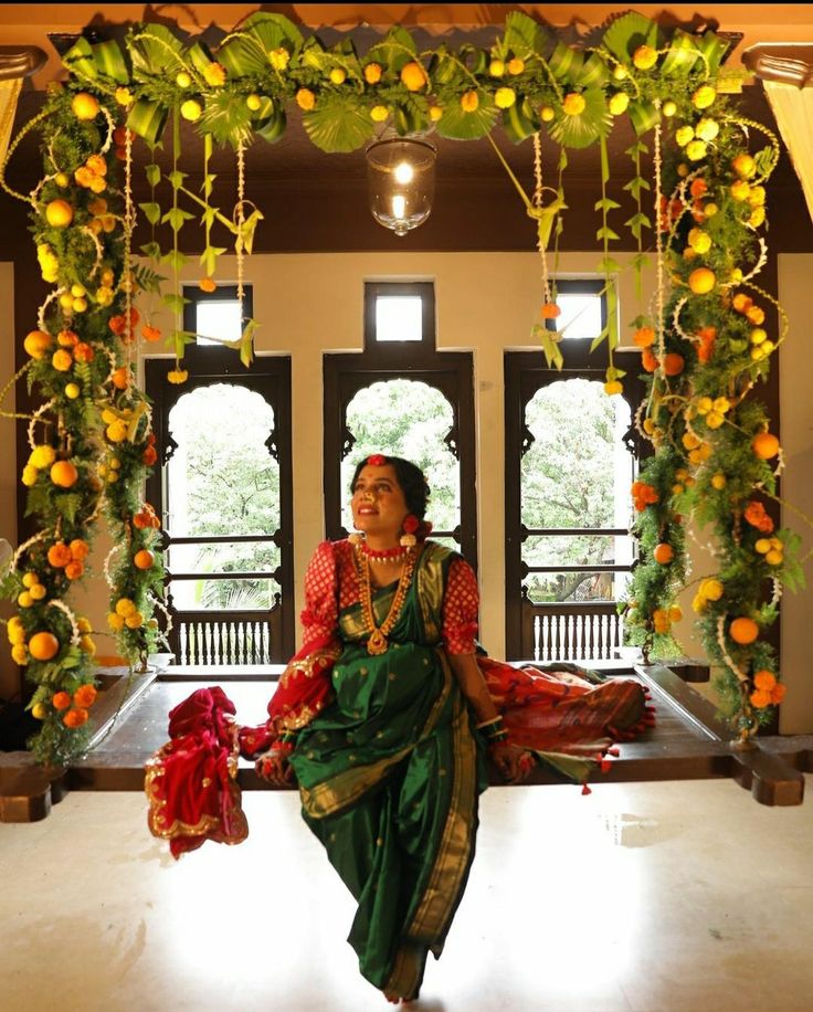 a woman sitting on a bench in front of an archway decorated with oranges and greenery