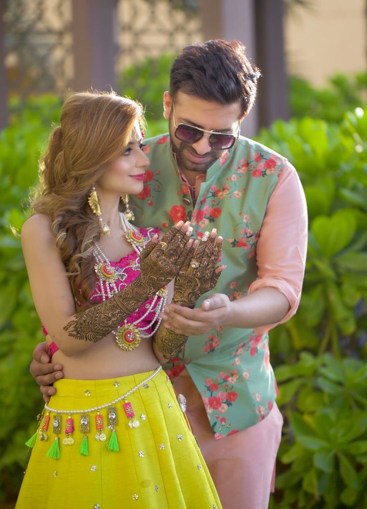 a man standing next to a woman in a yellow skirt and green shirt with henna on