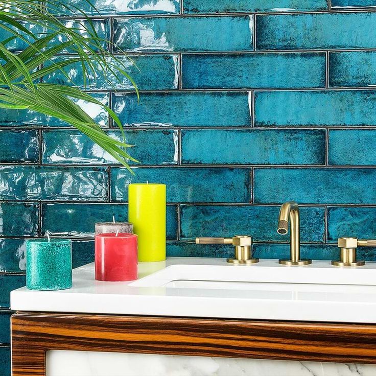 a bathroom sink sitting next to a green plant and blue tiled wall with gold faucets