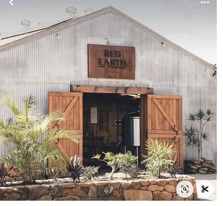 an image of a red earth storefront with plants and trees in the foreground