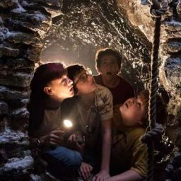 four children are sitting in a cave and one is holding a light up to their face