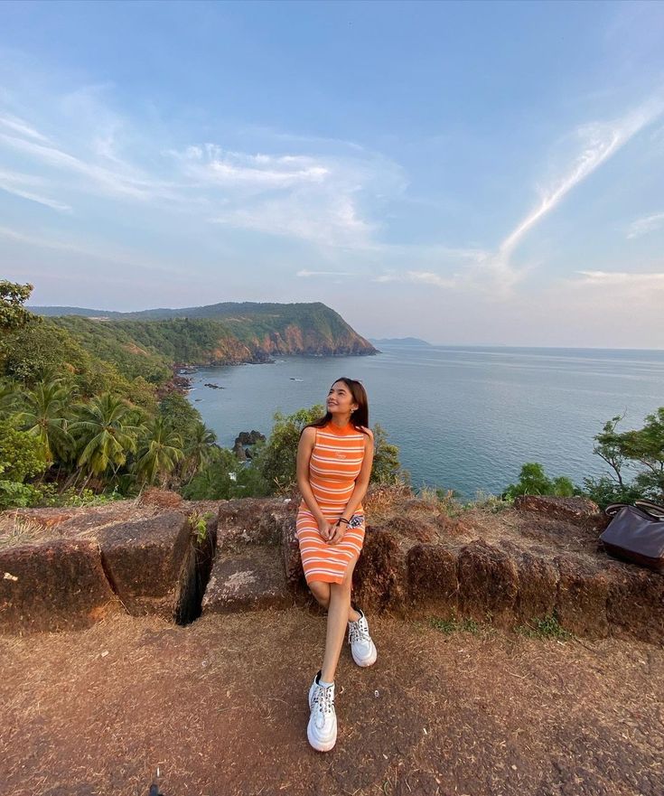 a woman sitting on the edge of a cliff looking up at the sky and water