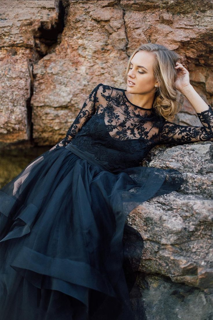 a woman sitting on top of a rock next to a river wearing a black dress