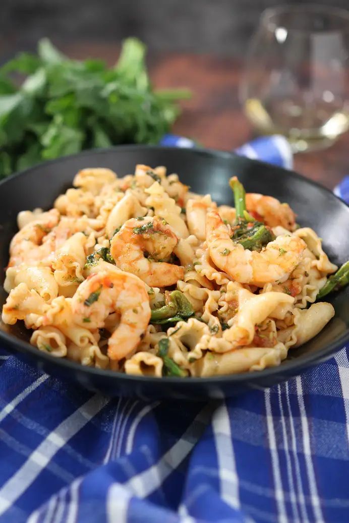 pasta with shrimp and asparagus in a black bowl on a blue checkered tablecloth