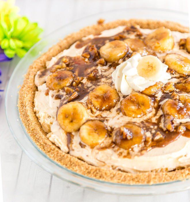 a pie with bananas and whipped cream on top is sitting on a table next to flowers