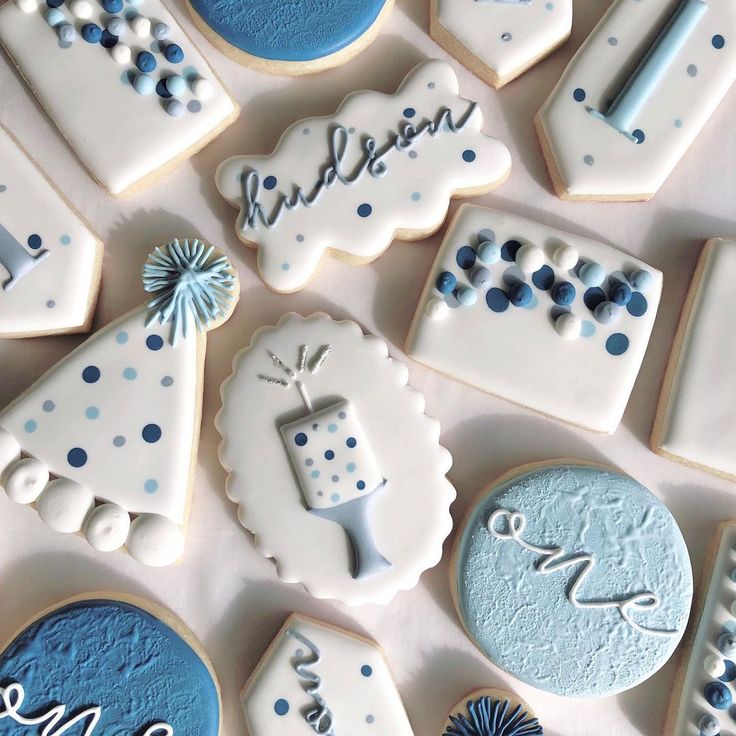 cookies decorated with blue and white icing are arranged on a table top for a baby's first birthday