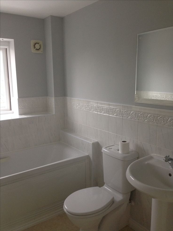 a white toilet sitting next to a bath tub in a bathroom under a window with a mirror above it