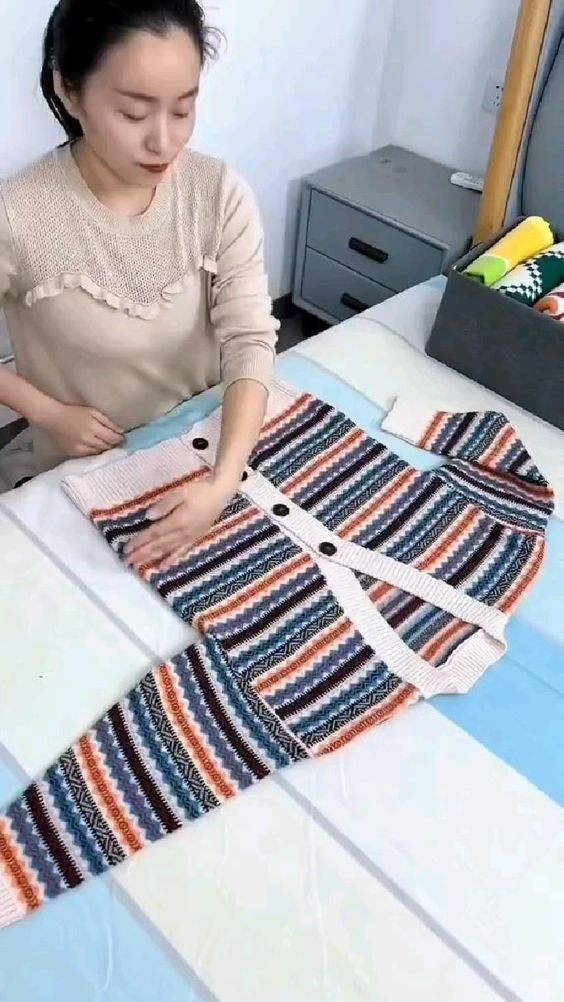 a woman sitting at a table working on some knitted clothing with scissors and thread