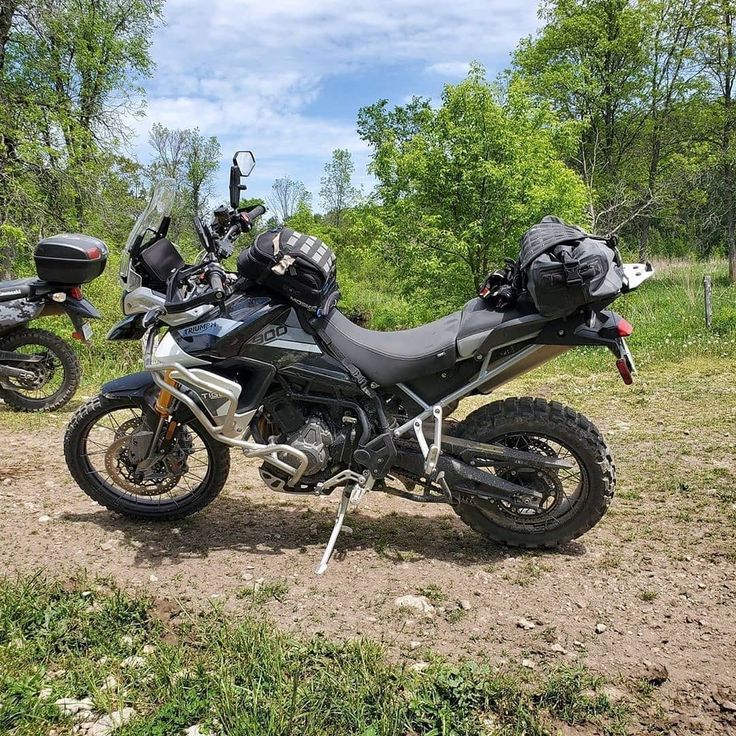 two motorcycles parked in the dirt near trees