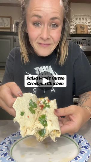 a woman holding up a burrito on top of a plate