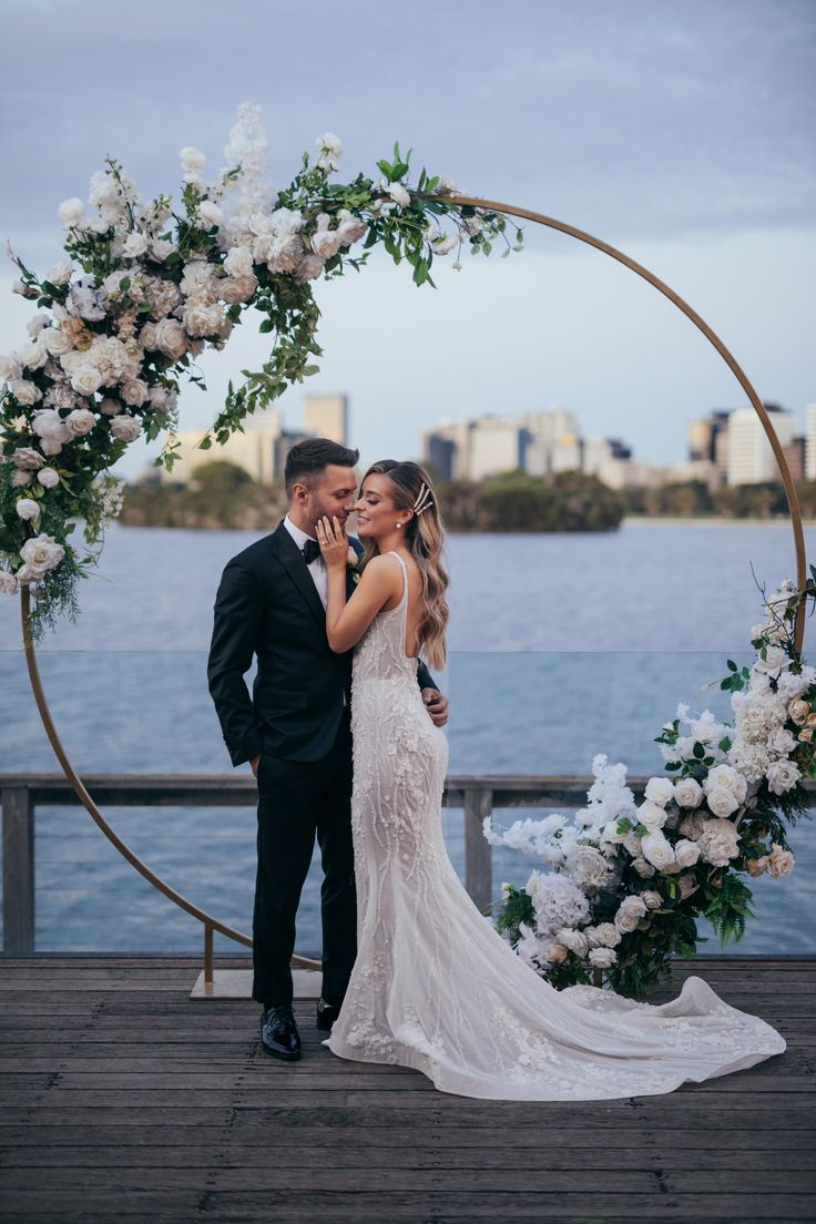 a bride and groom standing in front of a circular arch with white flowers on it