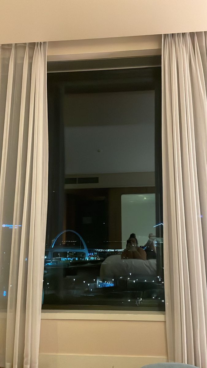 a person sitting on a bed in front of a window looking out at the city