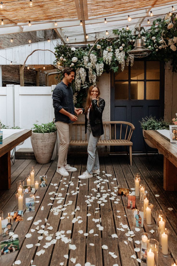 a man and woman standing on a wooden deck surrounded by white flowers with candles in front of them