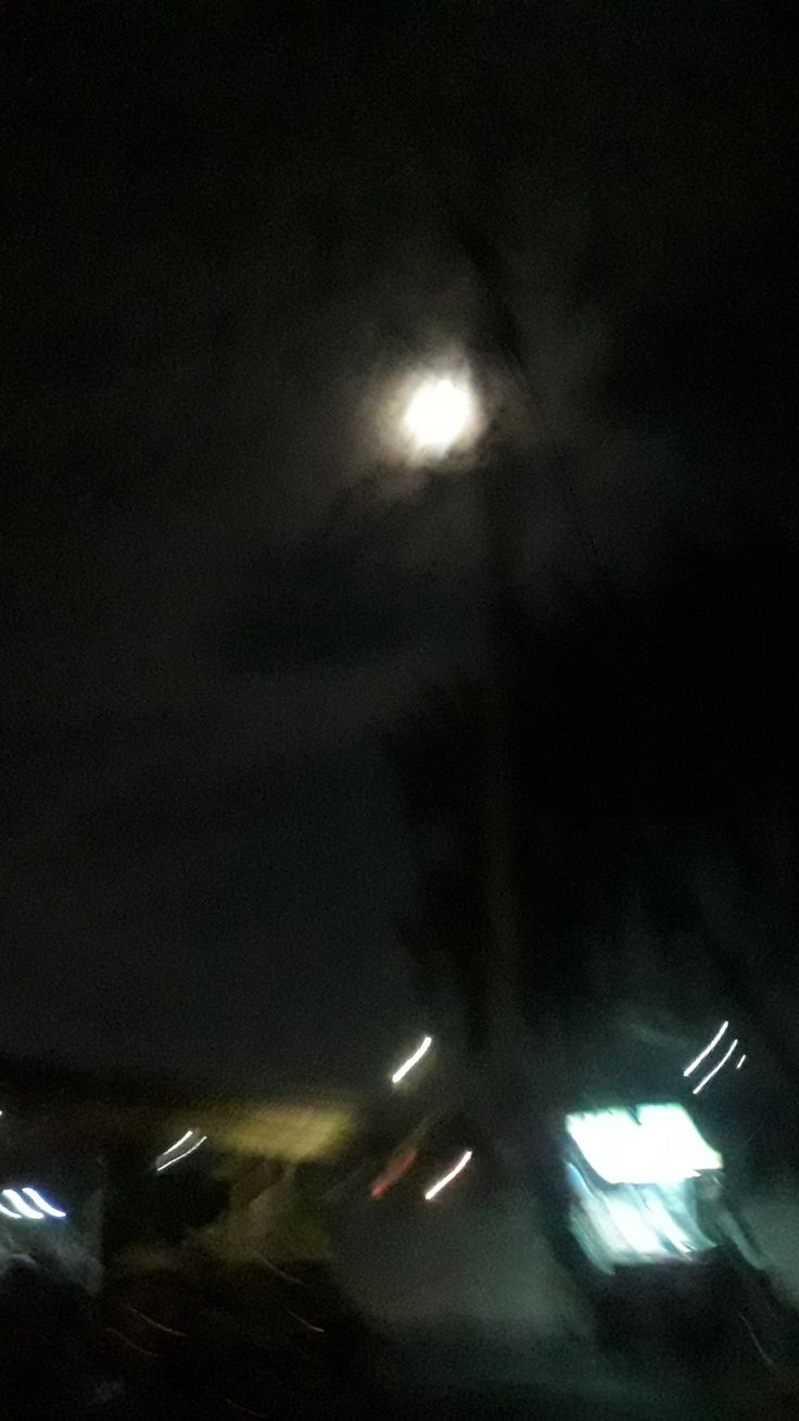 the moon is shining brightly in the dark sky over some buildings and cars at night