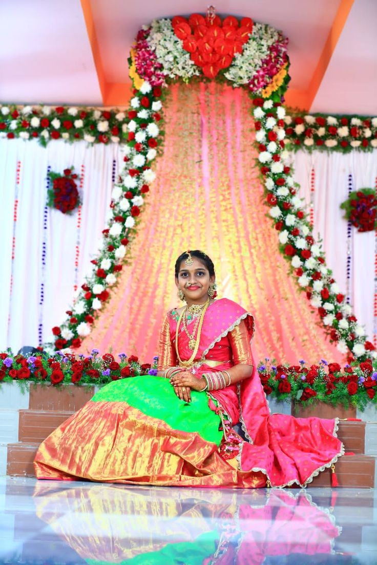 a woman sitting on the floor in front of a decorated stage with flowers and garlands