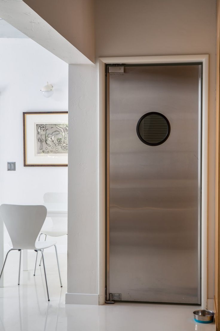 a stainless steel door in a white room with two chairs and a framed picture on the wall