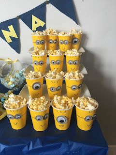 a blue table topped with yellow cups filled with popcorn covered in googly eyeballs